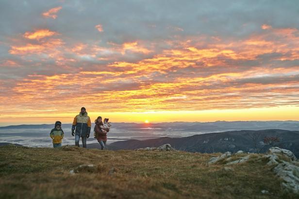 Eine Familie wandert bei Sonnenaufgang auf einem Hügel.