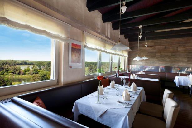 Ein Restaurant mit Tischen, gedeckt mit weißen Tischdecken und Blick auf eine grüne Landschaft.