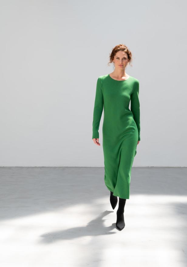 Eine Frau geht in einem grünen Kleid und schwarzen Stiefeln.