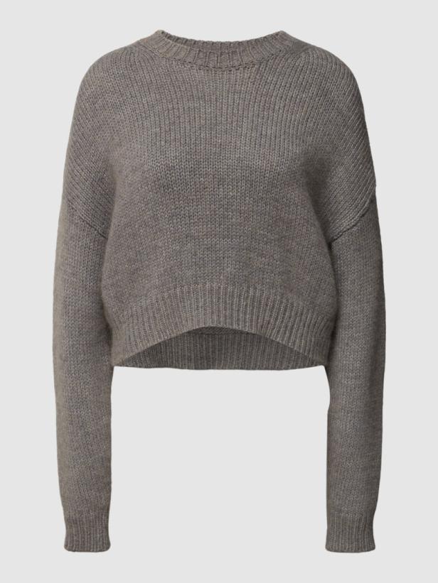 Ein grauer, kurz geschnittener Strickpullover mit langen Ärmeln.