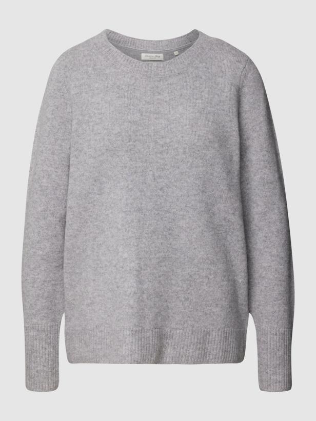 Ein grauer Strickpullover mit Rundhalsausschnitt vor einem hellen Hintergrund.