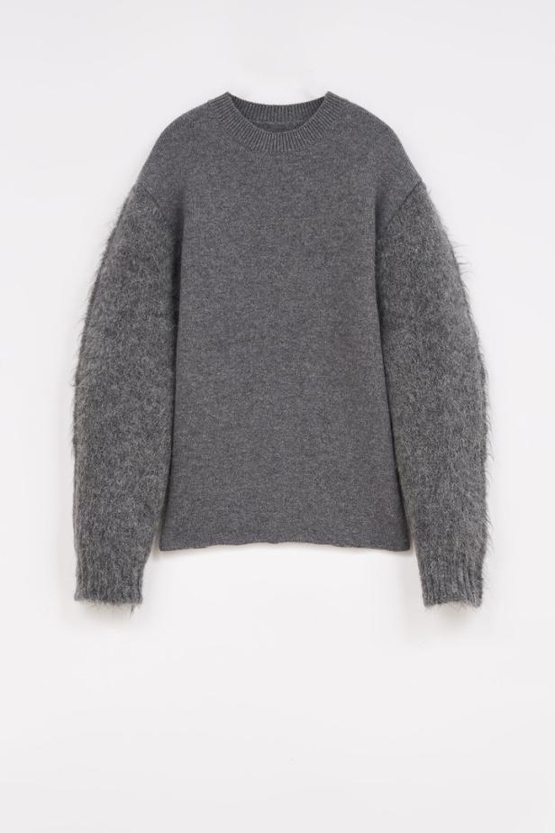 Ein grauer Pullover mit langen, zotteligen Ärmeln vor einem weißen Hintergrund.