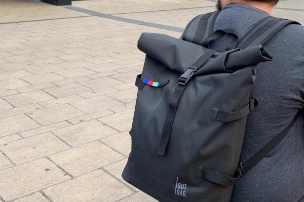 Eine Person trägt einen schwarzen Roll-Top-Rucksack der Marke „Got Bag“.