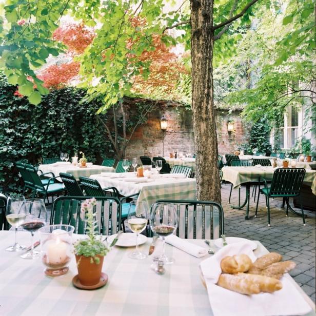 Einladende Tische im Freien unter Bäumen in einem Restaurantgarten.