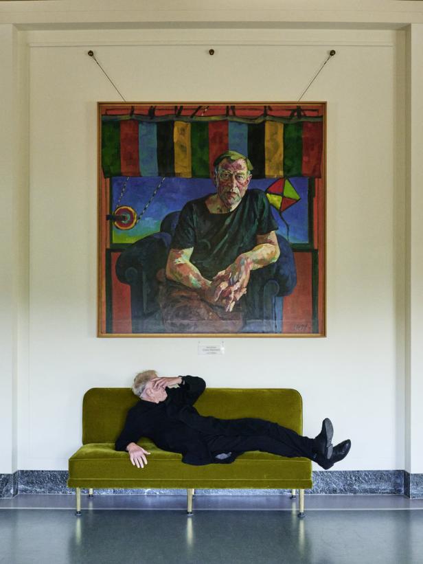 Ein Mann liegt auf einer grünen Couch unter einem Porträtgemälde.