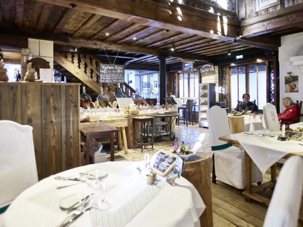 Innenansicht eines Restaurants mit Holzbalkendecke und gedeckten Tischen.