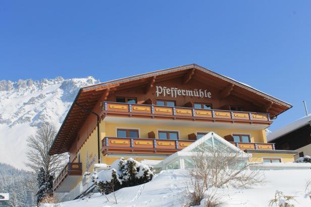 Das Aparthotel Pfeffermühle vor einer verschneiten Bergkulisse.