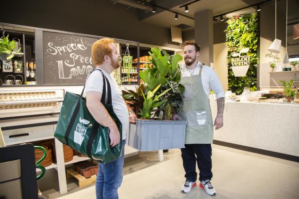 Ein Kunde kauft in einem Blumengeschäft eine Kiste mit Zimmerpflanzen.