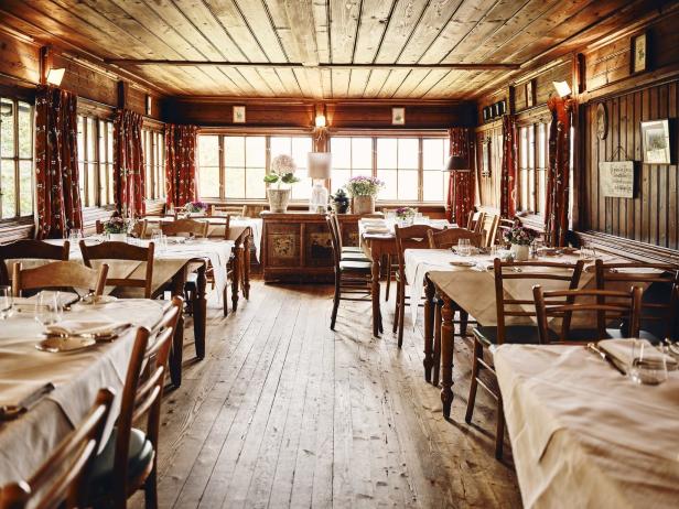 Ein Speisesaal mit Holzwänden, Tischen mit weißen Tischdecken und Blumenarrangements.