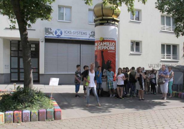Eine Gruppe von Menschen steht vor einem Plakat für das Theaterstück „Don Camillo und Peppone“.