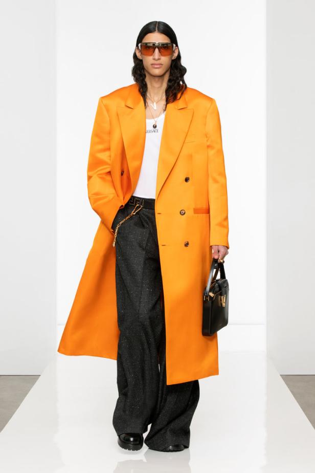 Ein Model in einem orangefarbenen Mantel und einer schwarzen Handtasche auf dem Laufsteg.