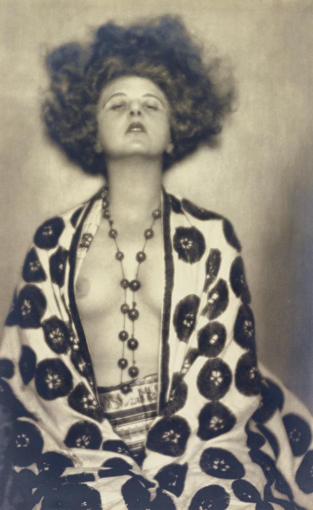 Eine Frau mit lockigem Haar und einer Halskette trägt einen gemusterten Kimono.