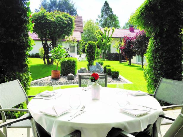 Ein gedeckter Tisch auf einer Terrasse mit Blick auf einen gepflegten Garten.