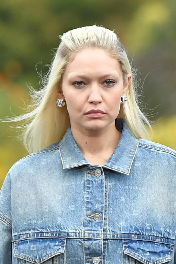 Gigi Hadid trägt eine Jeansjacke mit Givenchy-Logo und auffällige Ohrringe.