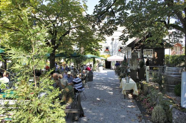 Ein Biergarten mit vielen Gästen unter schattenspendenden Bäumen.