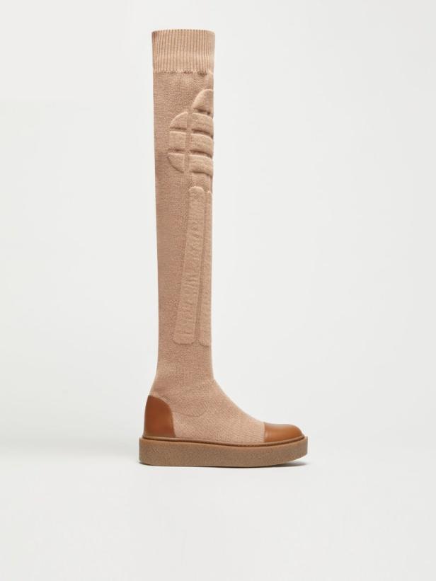 Ein beiger, kniehoher Stiefel mit Ledereinsätzen an Zehen und Ferse steht vor einem weißen Hintergrund.