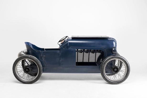 Ein blaues, antikes Spielzeugauto steht vor einem weißen Hintergrund.