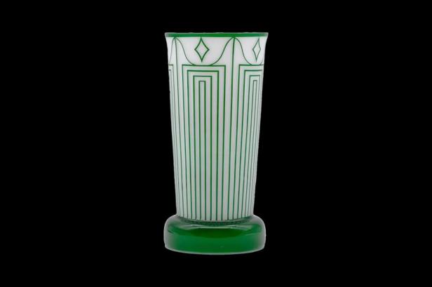 Eine weiße Vase mit grünen Art-Déco-Mustern auf einem schwarzen Hintergrund.