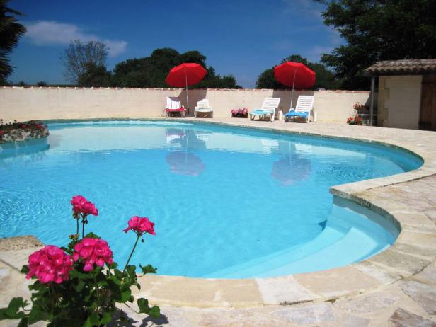 Ein Swimmingpool mit Liegestühlen und roten Sonnenschirmen an einem sonnigen Tag.