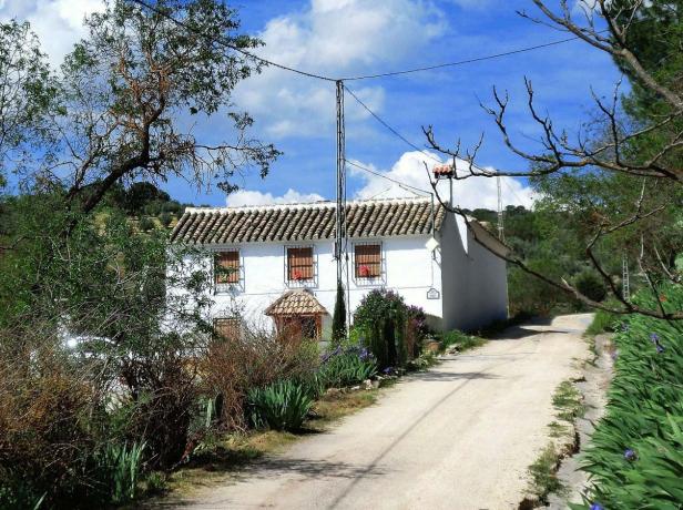 Ein weißes Haus mit Ziegeldach an einer unbefestigten Straße.