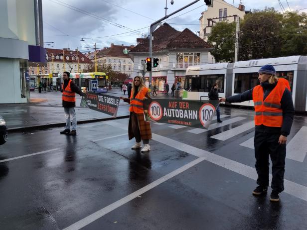 Aktivisten der „Letzten Generation“ blockieren eine Straßenbahnhaltestelle mit Protestbannern.