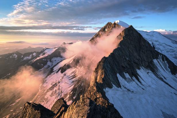 Die schneebedeckten Berggipfel ragen in den bewölkten Himmel.