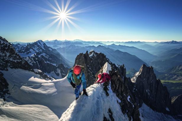 Zwei Bergsteiger erklimmen einen schneebedeckten Gipfel unter strahlendem Sonnenschein.