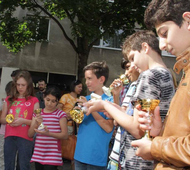 Eine Gruppe von Kindern hält goldene Trophäen in den Händen.