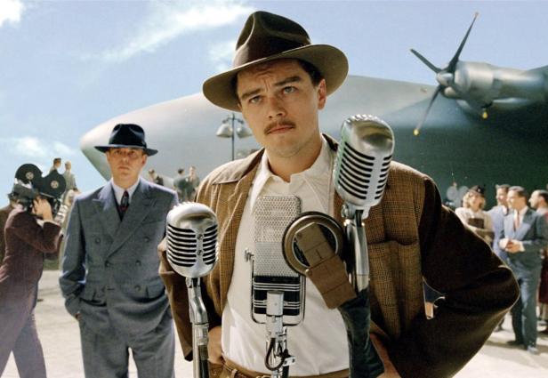 Leonardo DiCaprio als Howard Hughes vor Mikrofonen und dem „Hercules“-Flugzeug.