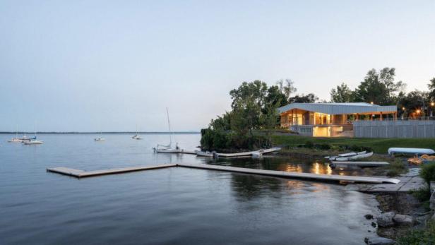 Ein modernes Gebäude am Ufer eines Sees mit mehreren Segelbooten.