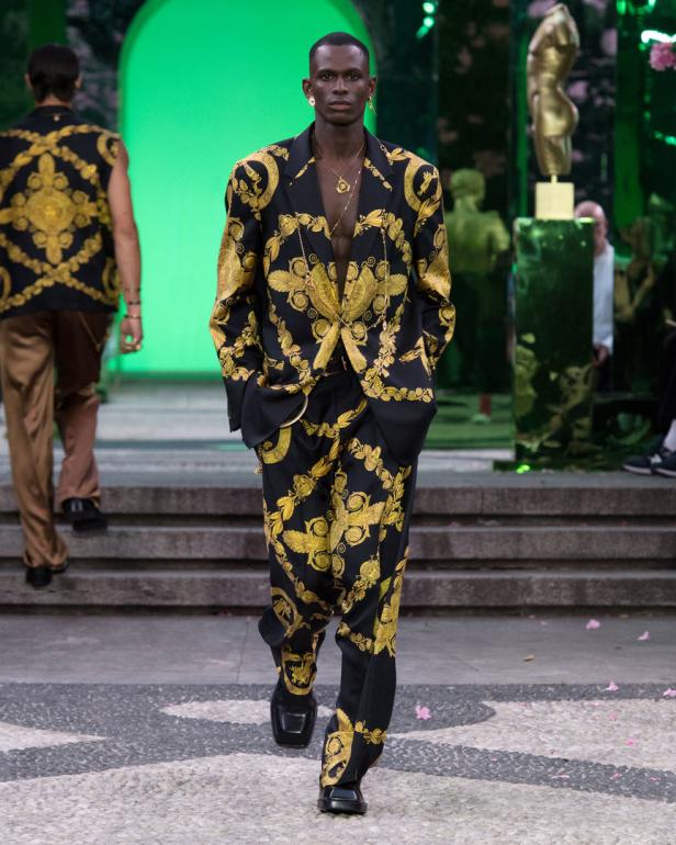 Ein Mann in einem Versace-Anzug mit goldenem Muster auf einem Laufsteg.