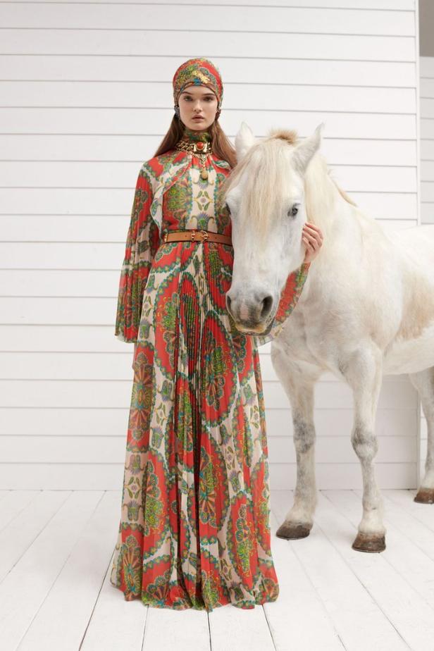 Eine Frau in einem gemusterten Kleid und Turban posiert mit einem weißen Pferd.