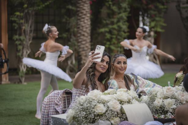Zwei Frauen machen ein Selfie, während im Hintergrund Ballerinen tanzen.