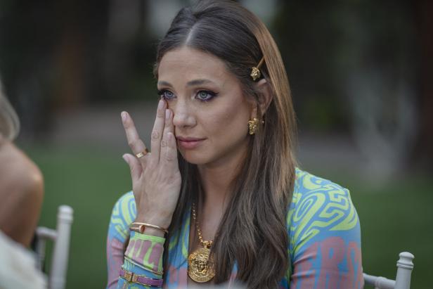 Eine Frau mit Versace-Schmuck wischt sich eine Träne aus dem Gesicht.
