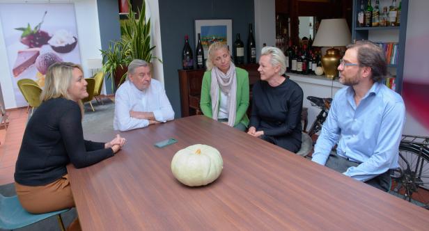 Fünf Personen sitzen an einem Tisch mit einem Kürbis in der Mitte.