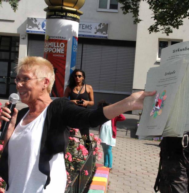 Eine Frau spricht in ein Mikrofon und hält Urkunden in der Hand.