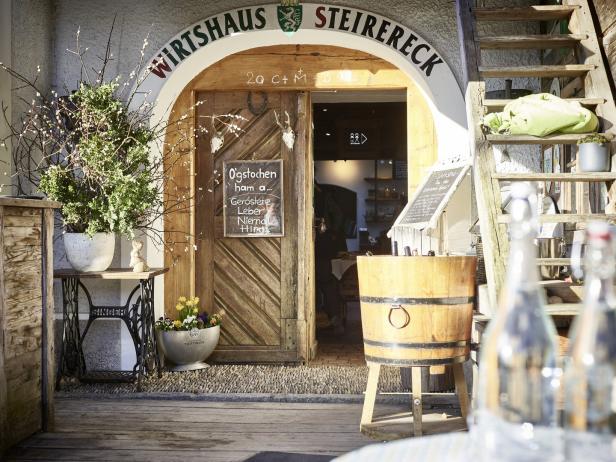 Der Eingang zum „Wirtshaus Steirereck“ mit rustikalen Dekorationen und handgeschriebenen Schildern.