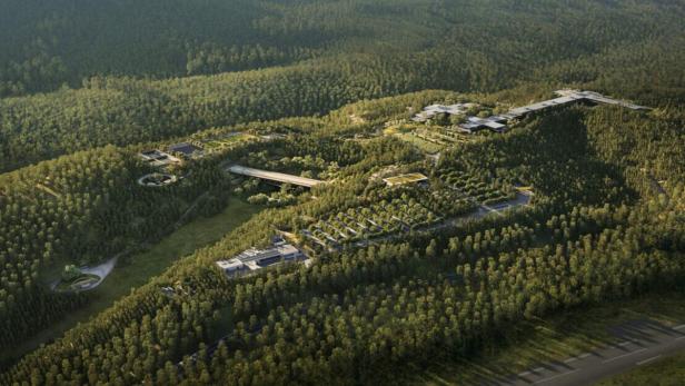 Luftaufnahme einer im Wald eingebetteten Wohnanlage mit mehreren Gebäuden und einer Brücke.