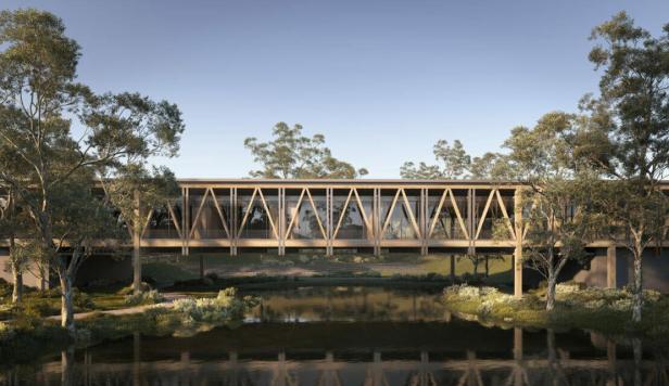 Eine moderne Holzbrücke überspannt einen ruhigen Fluss, umgeben von Bäumen.