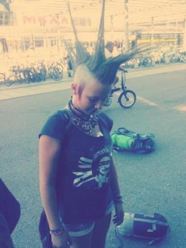 Eine junge Frau mit Irokesenschnitt und Punk-Kleidung steht auf der Straße.