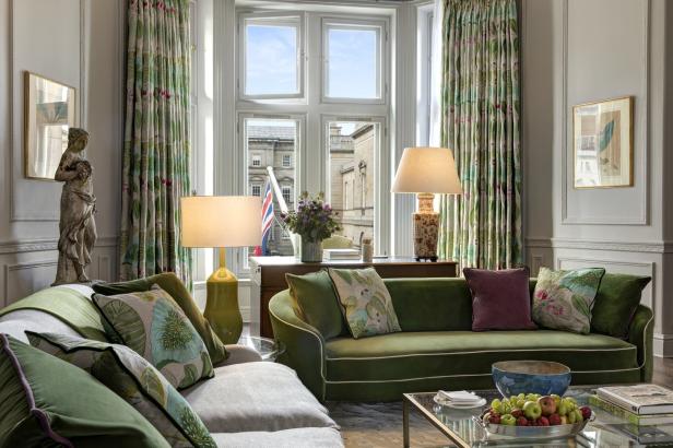 Ein Wohnzimmer mit grünen Sofas, floralen Vorhängen und Blick auf ein Gebäude mit einer britischen Flagge.