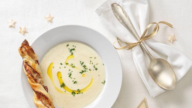 Eine Schüssel Cremesuppe mit einem Zimt-Prosciuttostangerl und Sternen verziert.