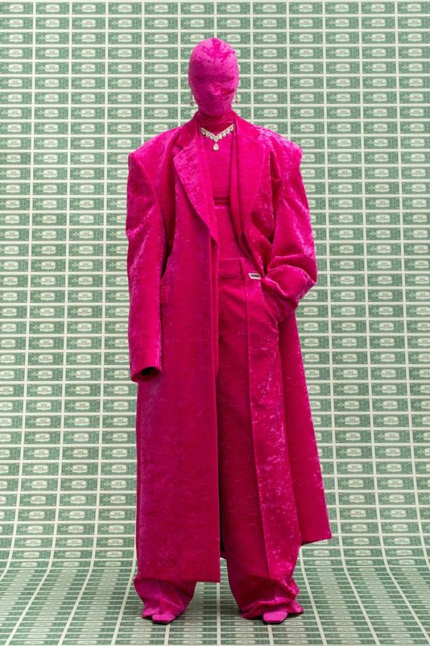Eine in pinkfarbenen Samt gehüllte Person mit Schmuck vor einem Hintergrund aus Dollarnoten.