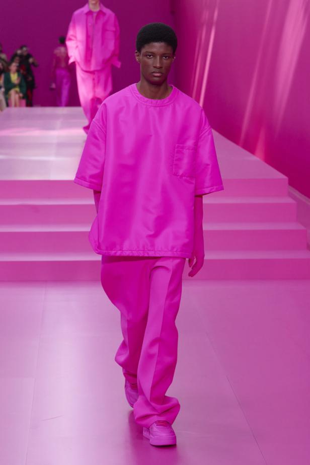 Ein dunkelhäutiger Mann in einem komplett pinken Outfit auf einem pinken Laufsteg.