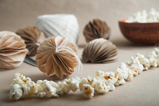 Eine Popcorngirlande liegt neben Papierornamenten und einer Schale Popcorn.