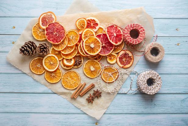 Getrocknete Orangen- und Grapefruitscheiben mit Zimtstangen, Sternanis, Tannenzapfen und Garn auf einem Tisch.