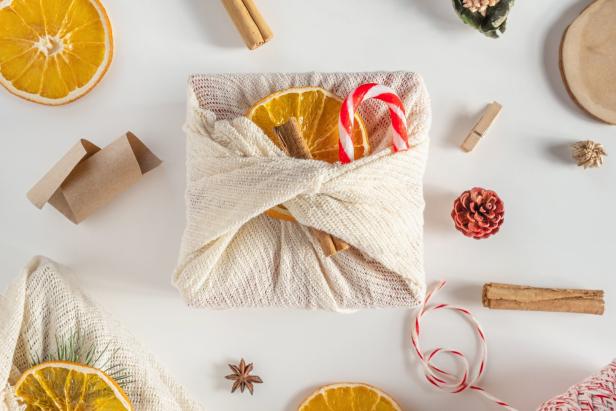 Ein Geschenk, verpackt in Stoff mit Orangenscheiben und einer Zuckerstange verziert, liegt auf einem Tisch.