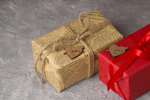 Zwei Geschenke, eines in Zeitungspapier und eines in rotes Papier verpackt, mit Schleifen und Holzherzen verziert.