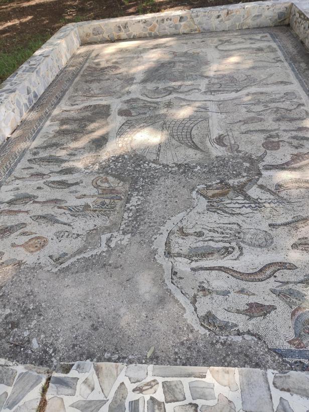 Ein antikes Mosaik zeigt eine maritime Szene mit Fischen und Schiffen.