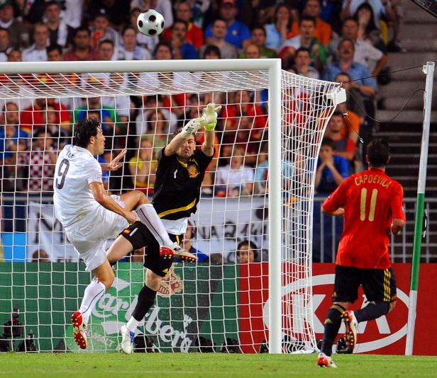 Ein Fußballspieler schießt auf das Tor, während der Torwart versucht, den Ball abzuwehren.